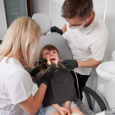 Dwóch stomatologów przeprowadzających przegląd dentystyczny u dziecka – rutynowa kontrola u młodego pacjenta