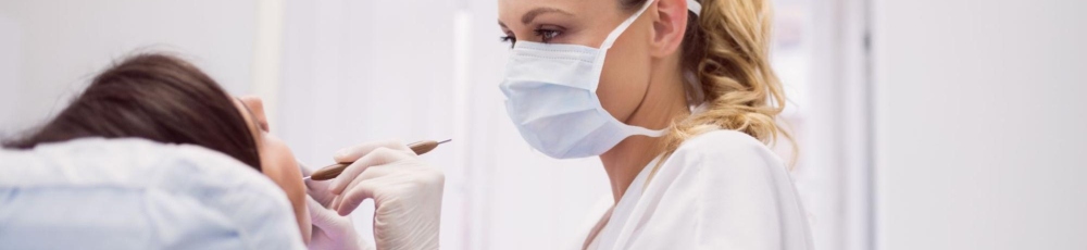 Dentystka w maseczce ochronnej podczas przeglądu jamy ustnej pacjentki – w trakcie wizyty kontrolnej